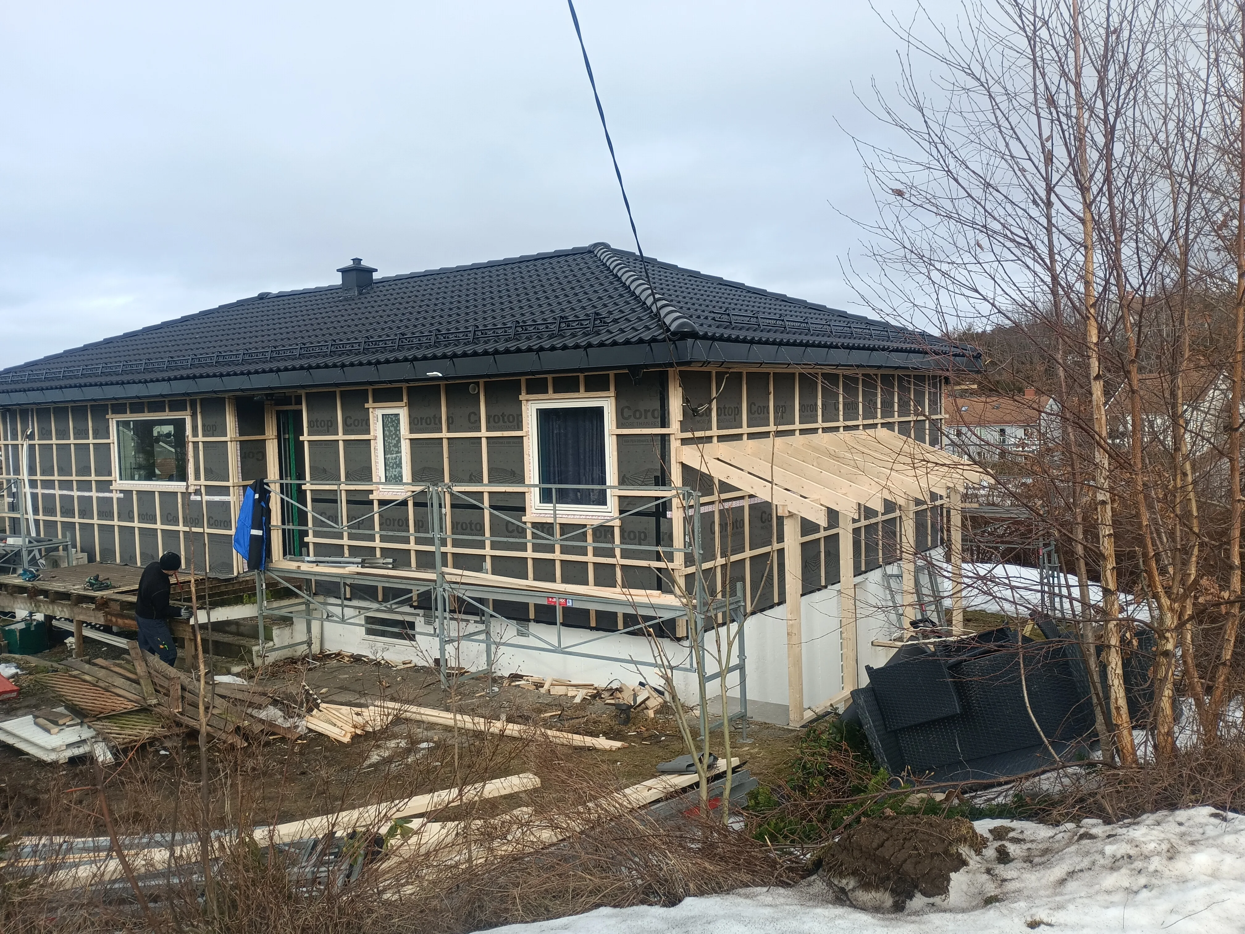 Hus med takomlegging, stillas og arbeider i bakgrunnen