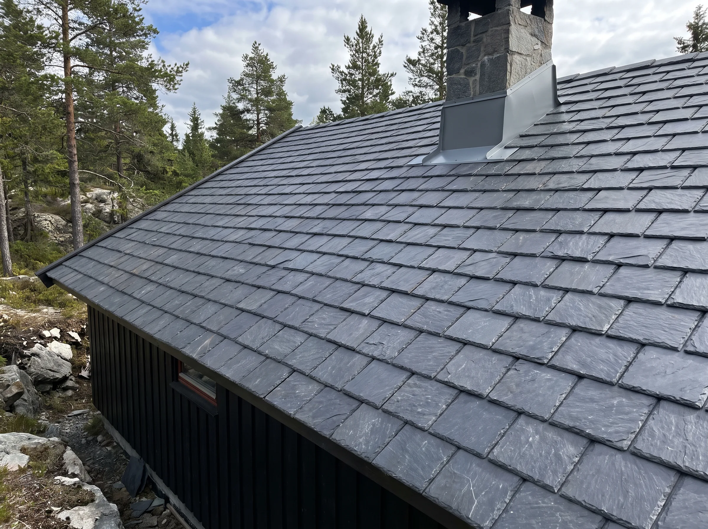Takstein på skråtak med pipe og skog i bakgrunnen