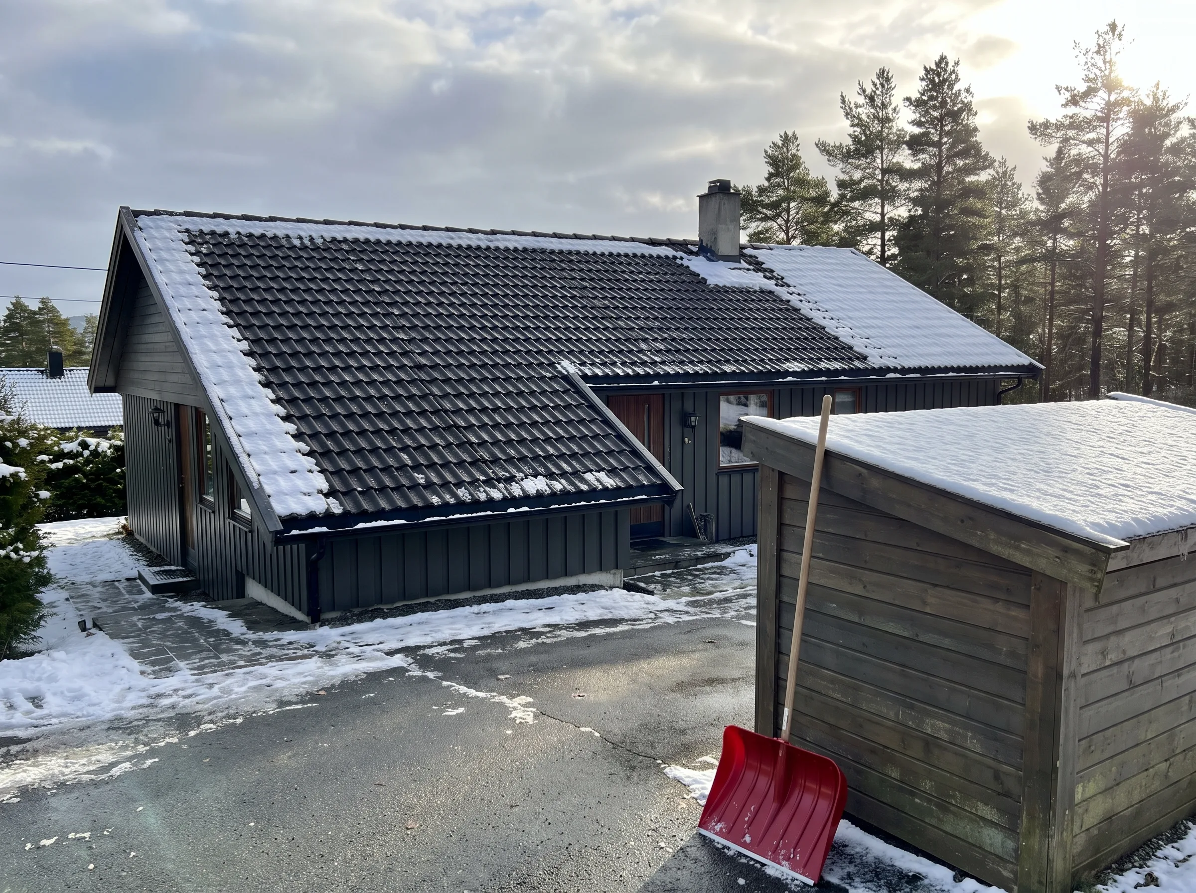 Hytte med skråtak dekket av takstein og snø, samt en snøspade i forgrunnen
