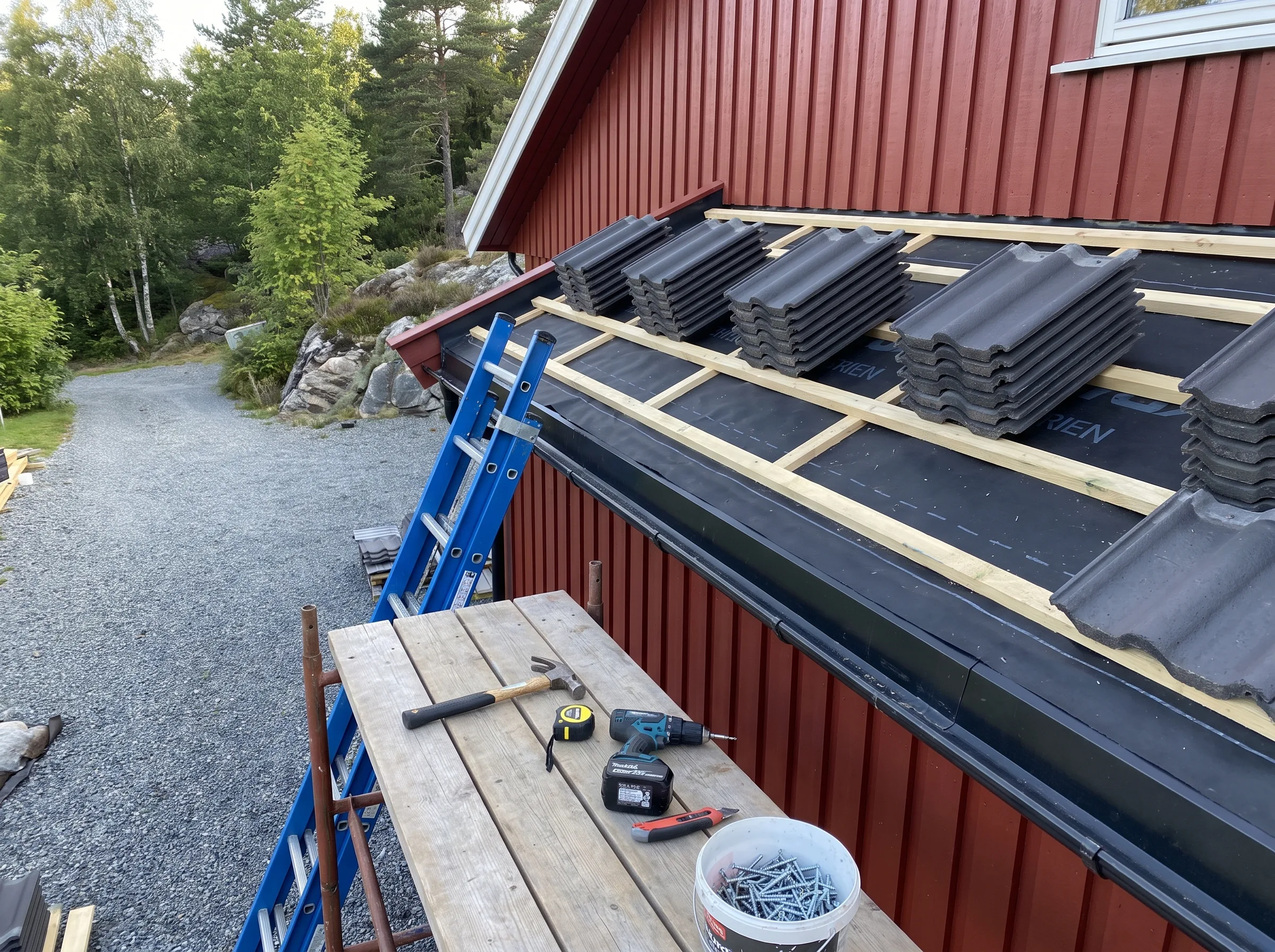 Montering av takstein på skråtak med verktøy og stige i bakgrunnen